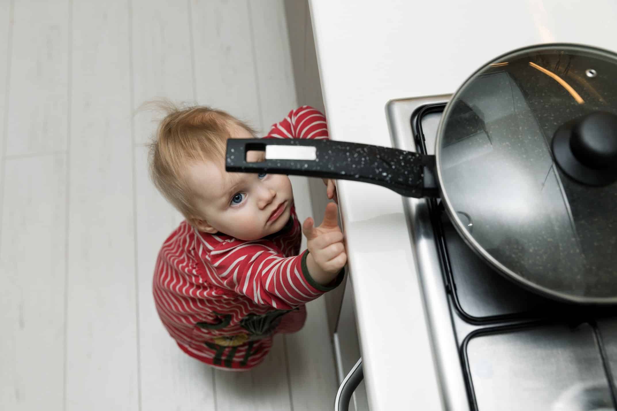 A toddler reaching for a pan on a stove